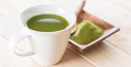 Kratom Tea in white glass next to a bowl of green powder